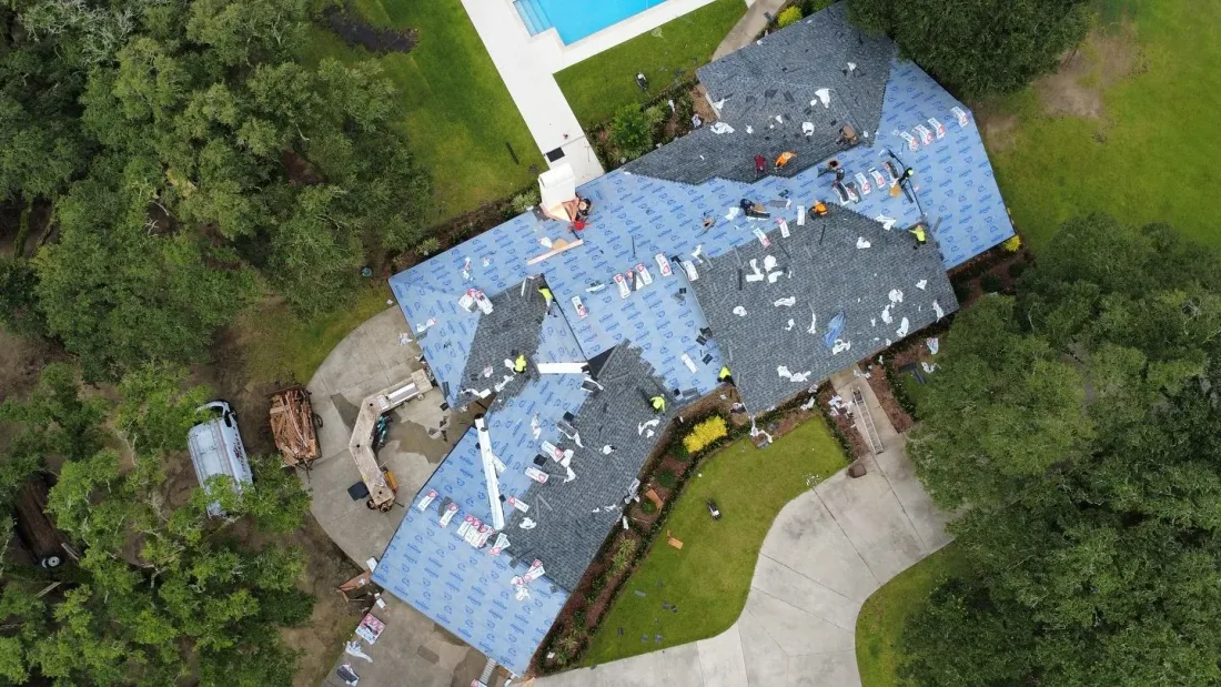 Aerial view of a large home mid-reroof with the crew working across the roof